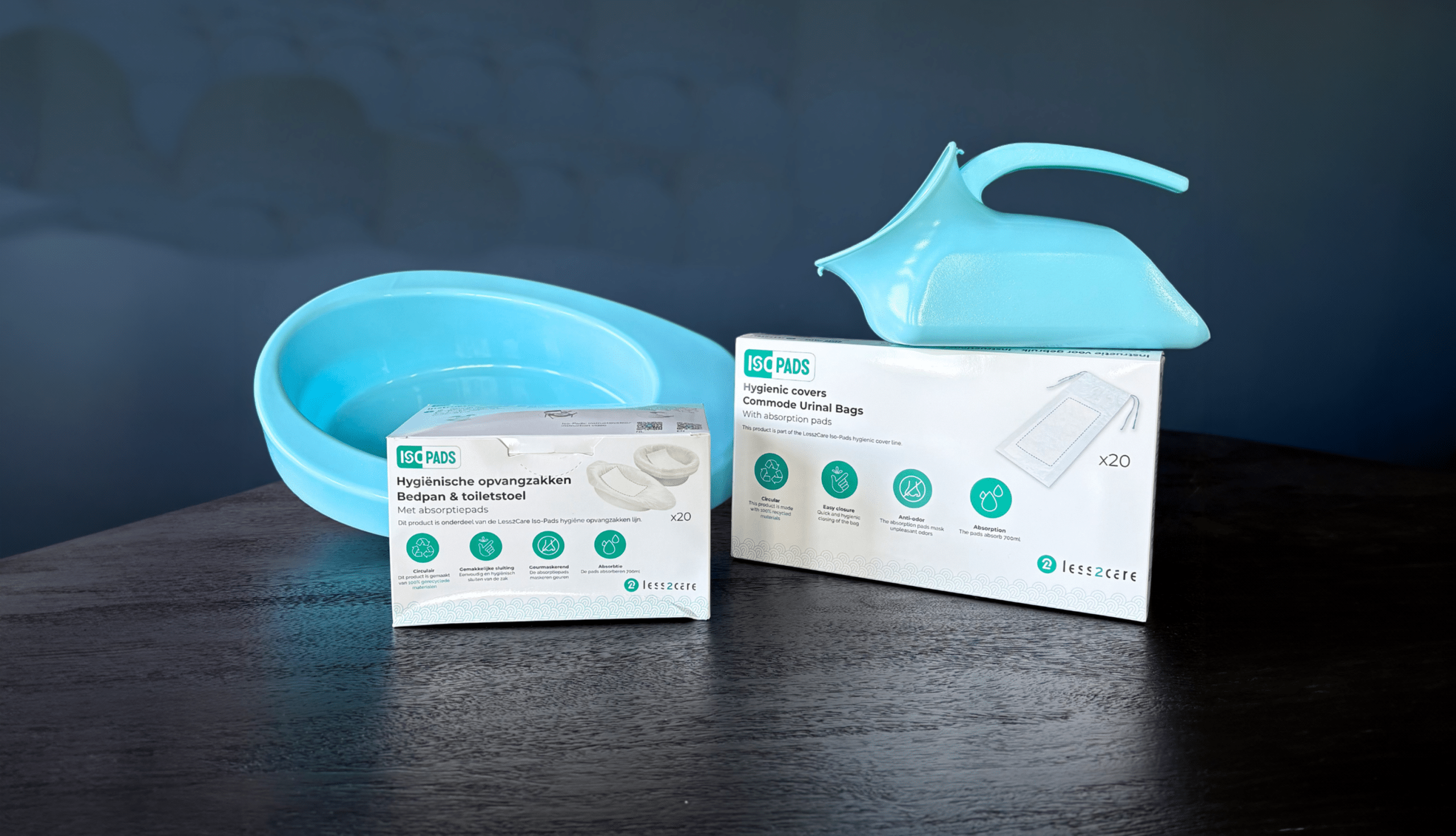 Twee medische hygiëneproducten, waaronder een turquoise bedpan en een urinepot, worden op een donkere tafel tentoongesteld, samen met hun verpakking – hygiënische hoezen en urinezakken voor de bedpan – waardoor de ervaring van NeboPlus met Less2Care tegen een donkerblauwe achtergrond goed tot zijn recht komt.